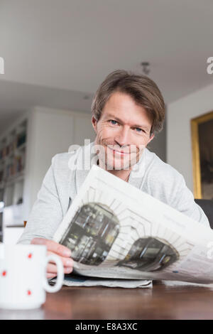 Portrait of mature man having coffee and reading newspaper, smiling Stock Photo