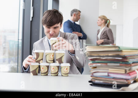 businessman building tower with coffee cups while businesspeople in background Stock Photo