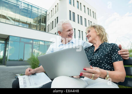 couple sitting on a bench, holding tablet computer and newspaper Stock Photo