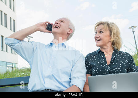 couple sitting on a bench, using tablet computer and smartphone Stock Photo