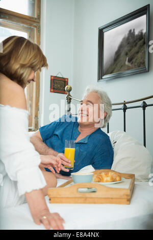 Couple having breakfast in bed, smiling Stock Photo