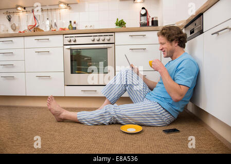 Man in pajama using digital tablet in kitchen Stock Photo