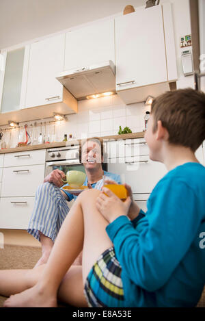 Happy father and son sitting on floor in kitchen Stock Photo