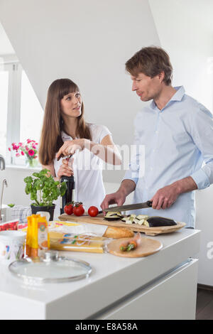 Mid adult woman opening wine bottle while mature man cutting vegetable Stock Photo