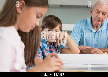 Children doing homework with their grandfather Stock Photo