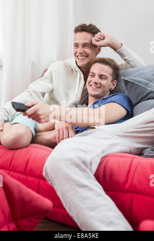 Homosexual couple watching tv with remote control in hand, smiling Stock Photo