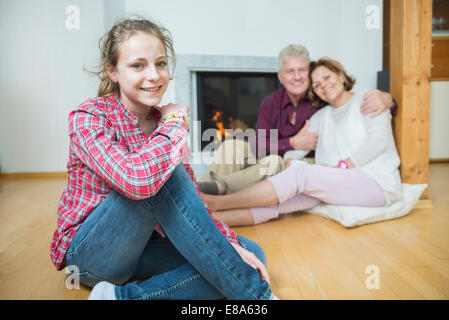 Granddaughter and grandparents sitting in front of fireplace, smiling Stock Photo