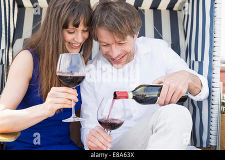 Couple having vine in roofed wicker beach chair, smiling Stock Photo