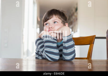 Boy leaning on wooden table, looking away Stock Photo