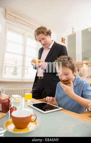 Boy using digital tablet during breakfast with father watching Stock Photo