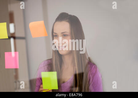 Young woman planning sticking post-its on glass Stock Photo