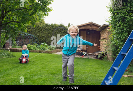 Older brother pulling sister on toy car in garden