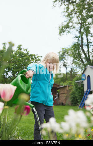 Young blonde girl watering flowers in garden Stock Photo