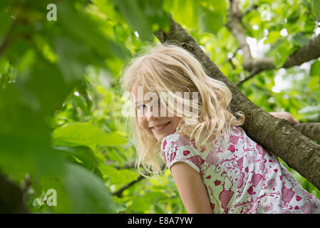 Young blonde girl in garden climbing tree Stock Photo