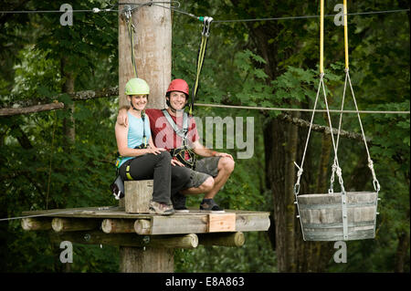 Young woman and young man sitting on stump, smiling Stock Photo