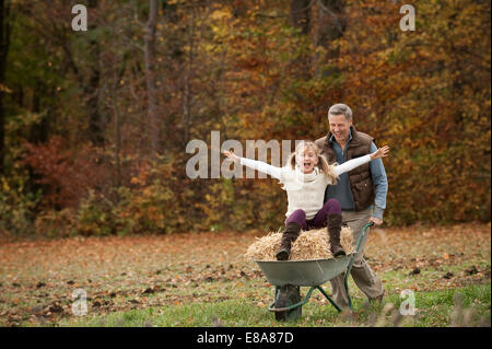 Father pushing happy daughter in wheelbarrow Stock Photo