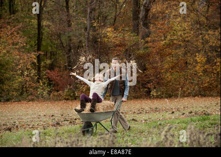 Father pushing happy daughter in wheelbarrow Stock Photo