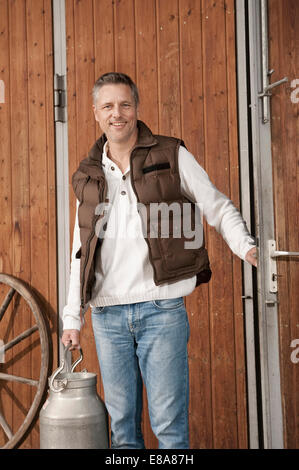 Smiling man holding milk churn on farm Stock Photo
