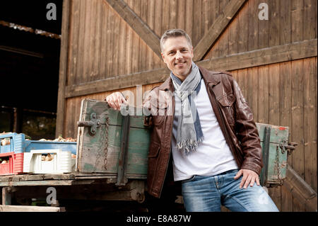 Smiling man leaning against trailer on farm Stock Photo