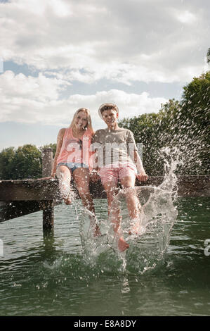 Teenage couple sitting on a jetty splashing water Stock Photo