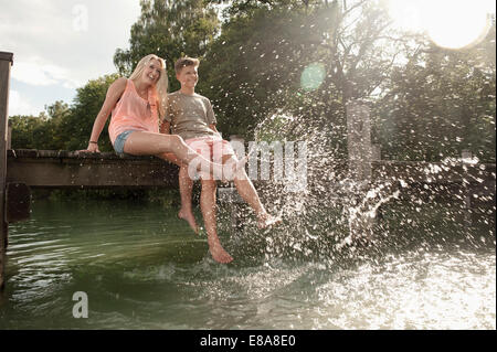 Teenage couple sitting on a jetty splashing water Stock Photo