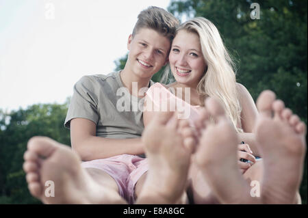 Smiling teenage couple sitting on a jetty at lake Stock Photo