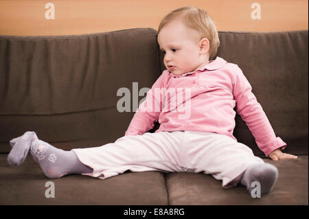 Tired baby girl 18 months old sitting on sofa Stock Photo