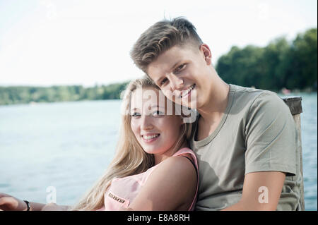 Portrait of teenage couple sitting on a jetty at lake Stock Photo