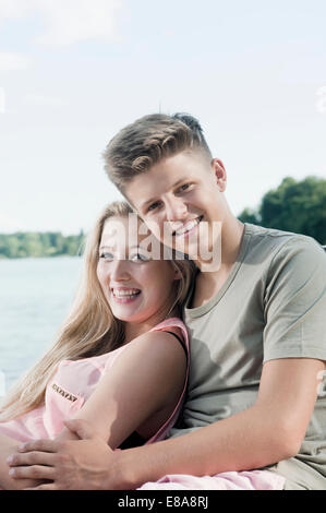Portrait of teenage couple sitting on a jetty at lake Stock Photo
