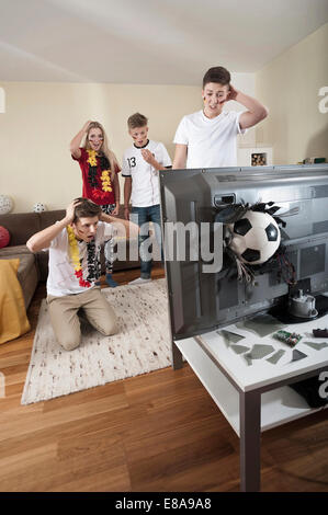 Teenage soccer fans in living room with ball demolishing TV Stock Photo