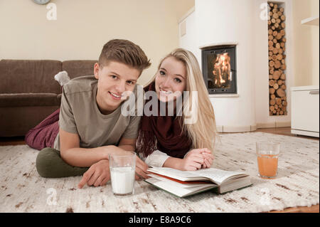 Teenage couple with book lying on carpet in front of fireside Stock Photo