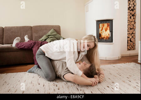 Teenage couple playfighting on carpet in front of fireside Stock Photo