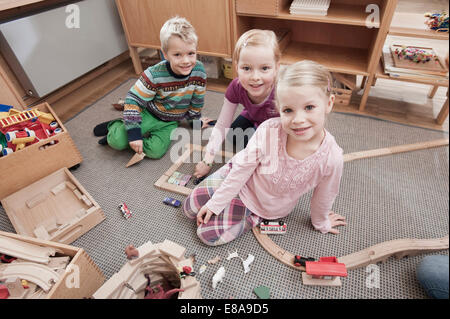Three little children with wooden building bricks in her kindergarten Stock Photo