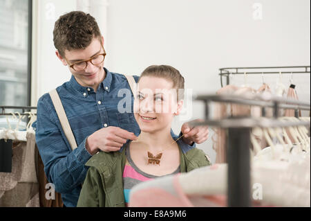 Young man putting necklace around young woman's neck at fashion store Stock Photo