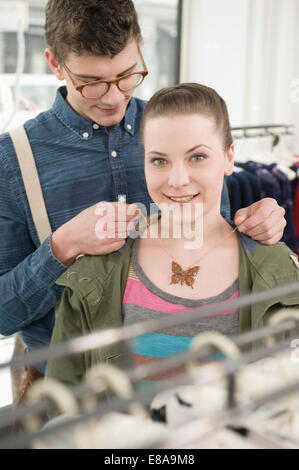 Young man putting necklace around young woman's neck at fashion store Stock Photo