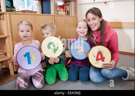 Group picture of female educator and three kids sitting in kindergarten Stock Photo