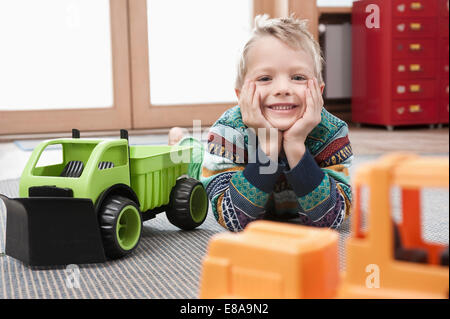 Portrait of smiling little boy with head in his hands lying on ground of his kindergarten Stock Photo