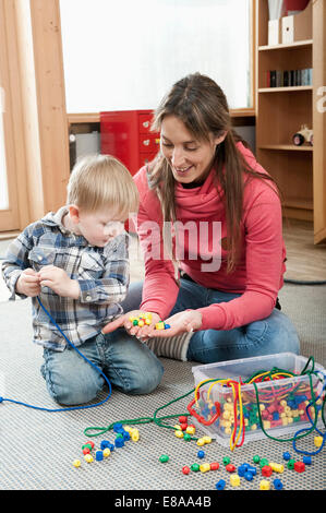 Female educator offering little boy wooden perls for making a necklace Stock Photo