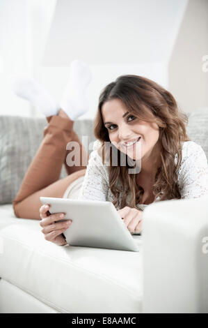 Portrait of smiling young woman with digital tablet lying on couch at home Stock Photo