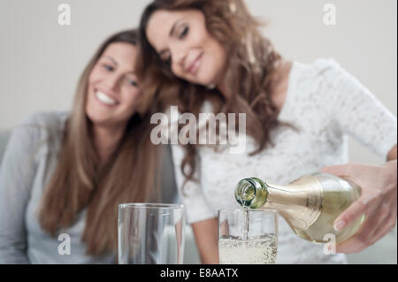 Young woman pouring champage into glasses while her female friend watching Stock Photo