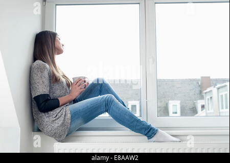 Young woman sitting on window sill at home Stock Photo