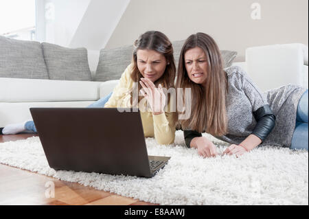 Two female friends lying side by side on carpet watching movie with laptop Stock Photo