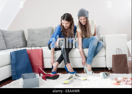 Two young female friends sitting side by side on couch at home trying on high heels Stock Photo