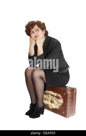 Young woman in thought sits on old scratched suitcase isolated on white background Stock Photo