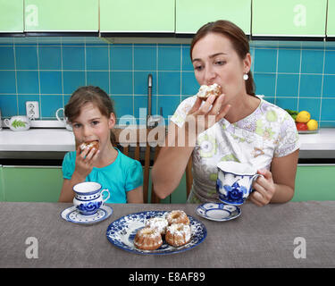 Mother and daughter eat muffins and drink tea in kitchen Stock Photo