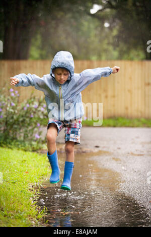 Boy in rubber boots jumping in rain puddle Stock Photo