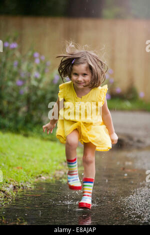 Child wearing yellow rain boots and jumping in puddle on a fall day ...