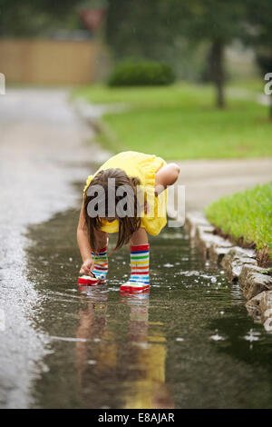 Girl wearing rubber boots picking leaf from rain puddle Stock Photo