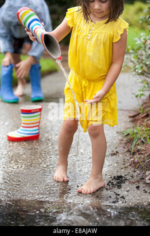 Girl pouring water from rubber boots into rain puddle Stock Photo