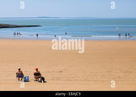 Middle aged couple sitting on folding chairs in the sunshine on fairly quiet beach. Stock Photo